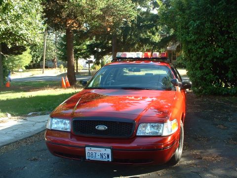 1999 Ford Crown Victoria - A red police car with a light bar is parked in a driveway on a sunny day.
