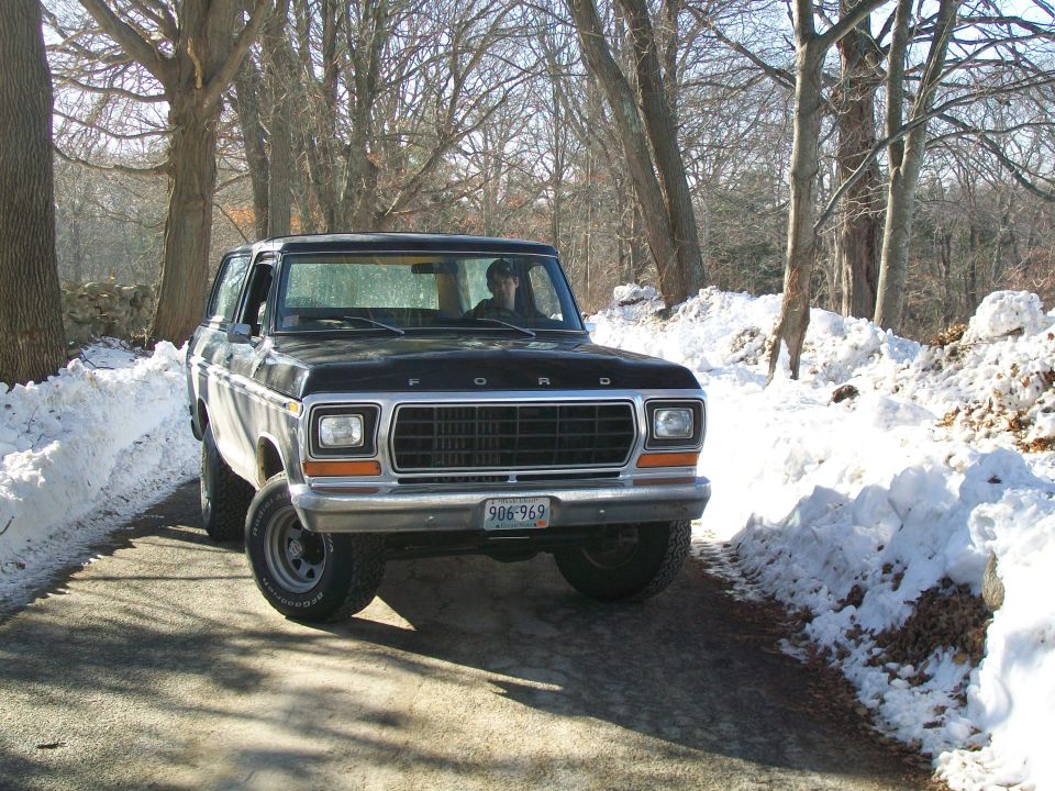 Black 1978 Ford Bronco driving on a snowy road, front view