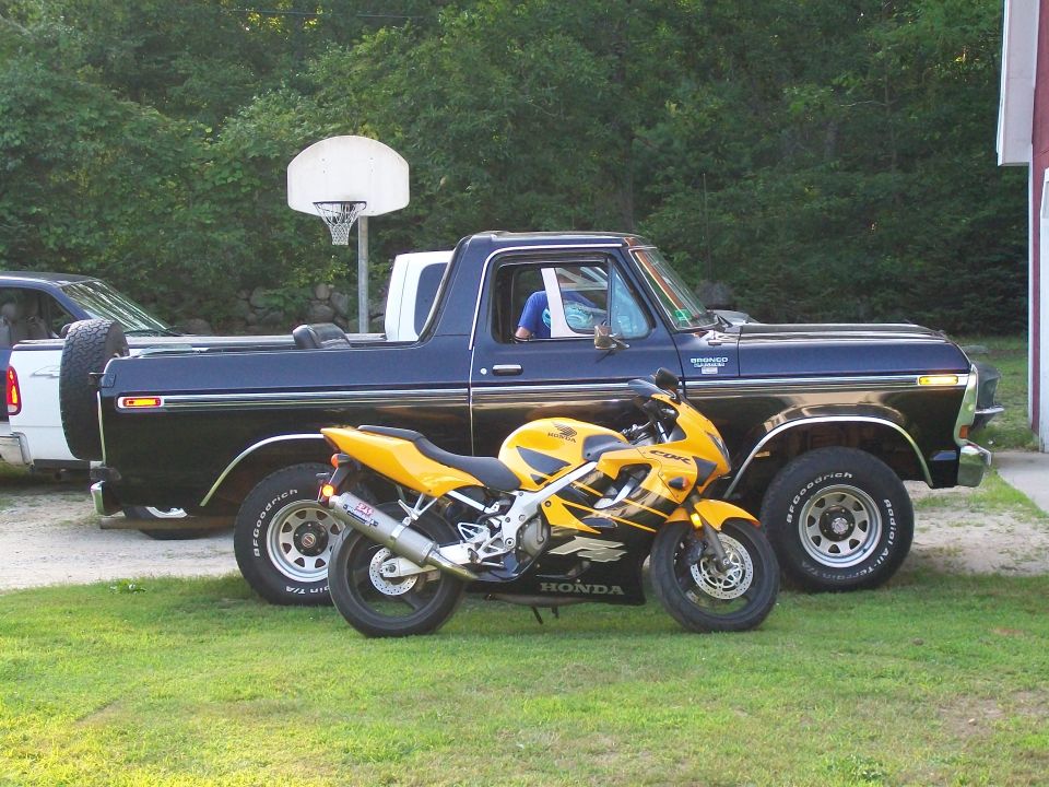 1978 Ford Bronco parked next to a yellow Honda CBR motorcycle. Another vehicle is partially visible to the left