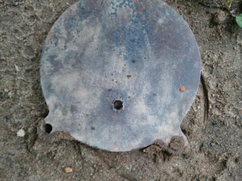 1985 Ford F-150 - A weathered round metal part, possibly a cover or plate, lies on the ground.
