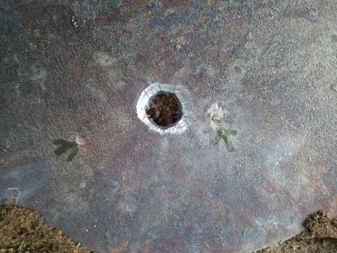 1985 Ford F-150 - Close-up of a heavily rusted metal plate showing a central hole and two green directional arrows.