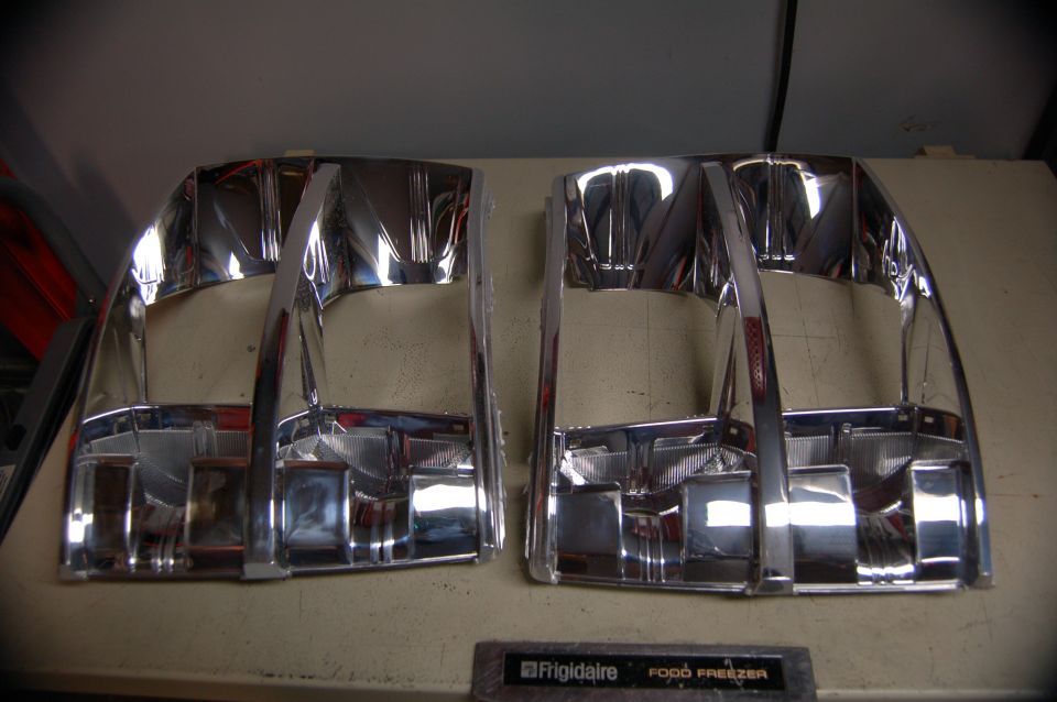 Two chrome headlight bezels, possibly for a truck, on a workbench
