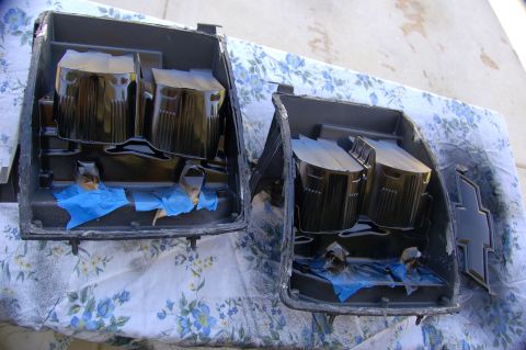 2007 Chevrolet Silverado 1500 - Two black plastic headlight housings are shown with blue tape applied to protect certain areas during a modification.