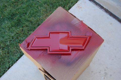 2007 Chevrolet Silverado 1500 - A red Chevrolet bowtie emblem is being spray painted on a cardboard box outdoors.