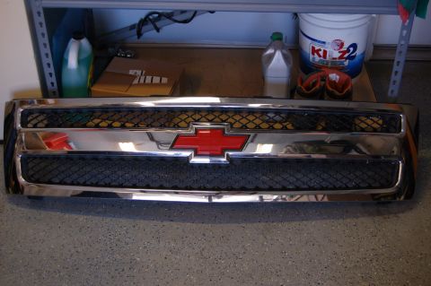 2007 Chevrolet Silverado 1500 - A chrome and black Chevrolet grille with a red bowtie emblem is displayed in front of shelves with supplies.