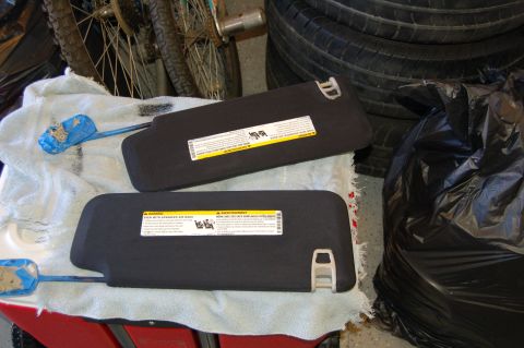 2007 Chevrolet Silverado 1500 - Two sun visors are displayed on a towel, with a pile of tires and a black trash bag in the background.
