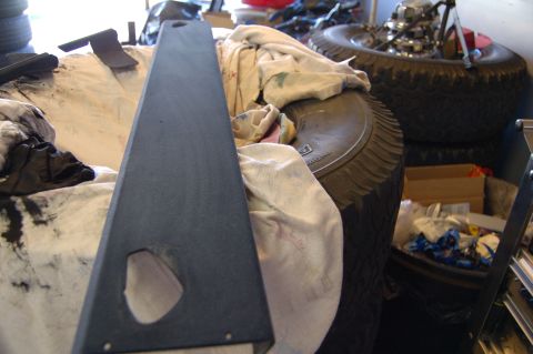 2007 Chevrolet Silverado 1500 - A dark gray interior shelf part with a large cutout is shown, placed on top of cloth and tires in a garage setting.