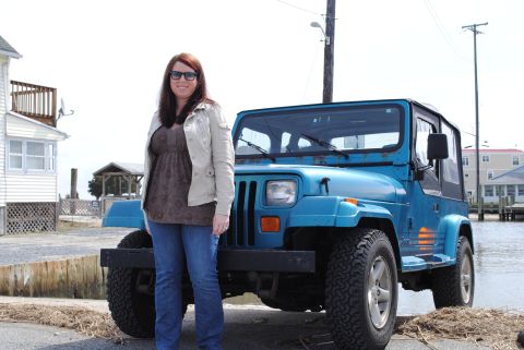 1991 Jeep YJ - A blue 1991 Jeep YJ is shown in a three-quarter front view, parked near a body of water with a woman standing next to it.