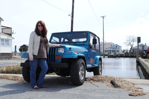 1991 Jeep YJ - A blue 1991 Jeep YJ is parked on a boat ramp, with a woman standing next to it and houses in the background.