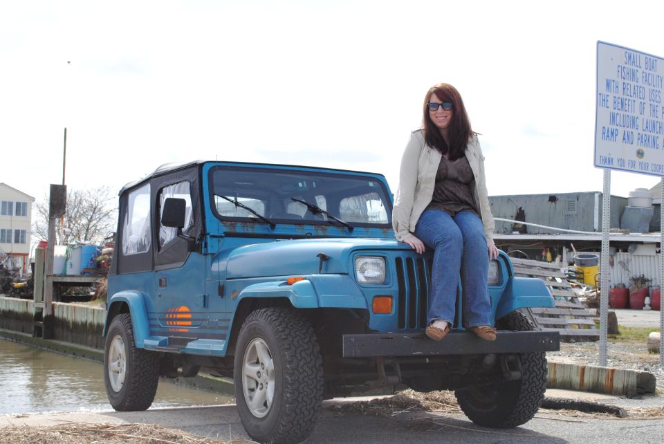1991 Jeep YJ with a woman sitting on the hood, parked near a body of water
