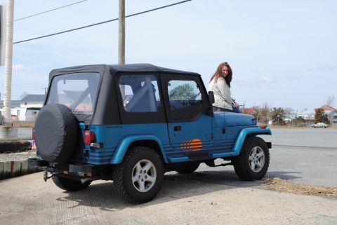1991 Jeep YJ - A blue 1991 Jeep Wrangler YJ is parked outdoors with a woman sitting on its hood.