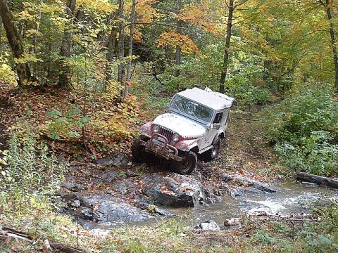 1978 Ford Bronco - A white Jeep CJ-7 navigates a rocky stream bed surrounded by autumn foliage.