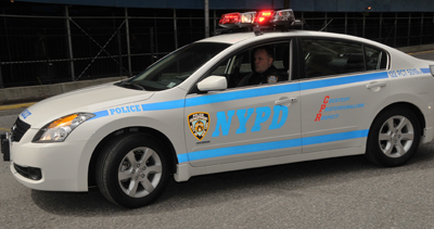 1991 Ford LTD Crown Victoria - A white NYPD police car with blue stripes and emergency lights is seen from the side.