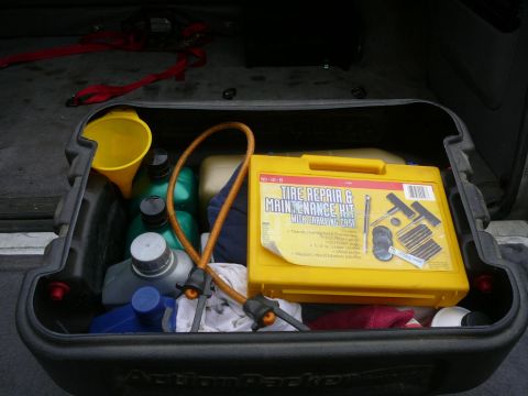 1988 Ford Bronco - A storage box in a vehicle contains various fluids, a funnel, and a tire repair kit.