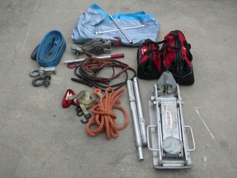 1988 Ford Bronco - A collection of vehicle recovery and maintenance tools, including tow straps, rope, jumper cables, a tarp, and a floor jack, laid out on a…