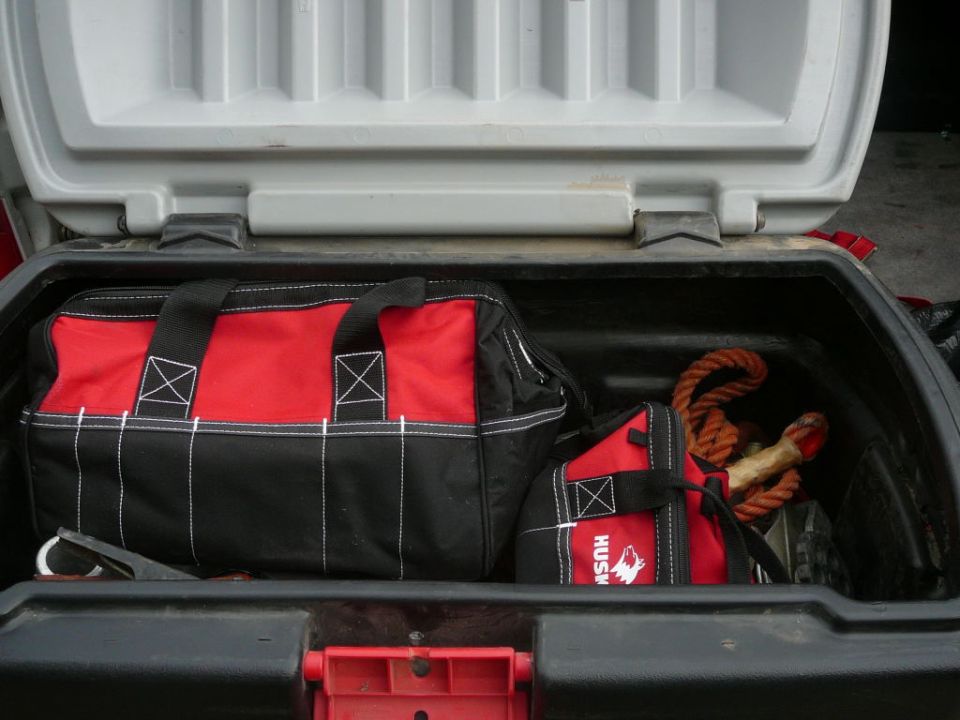 Two red and black tool bags and a coiled rope inside a black cargo box with a gray lid