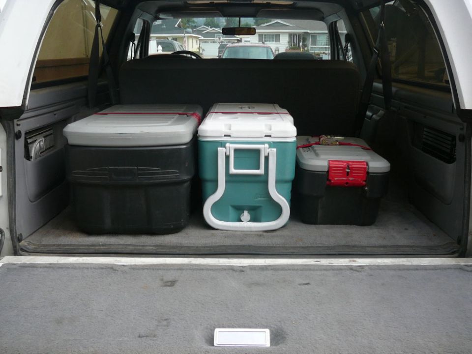 Interior cargo area of a white SUV with three coolers. The coolers are black, teal, and gray with red accents