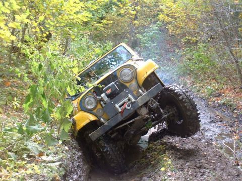1978 Ford Bronco - Off-road Jeep CJ navigating a muddy trail with dense foliage on the sides.