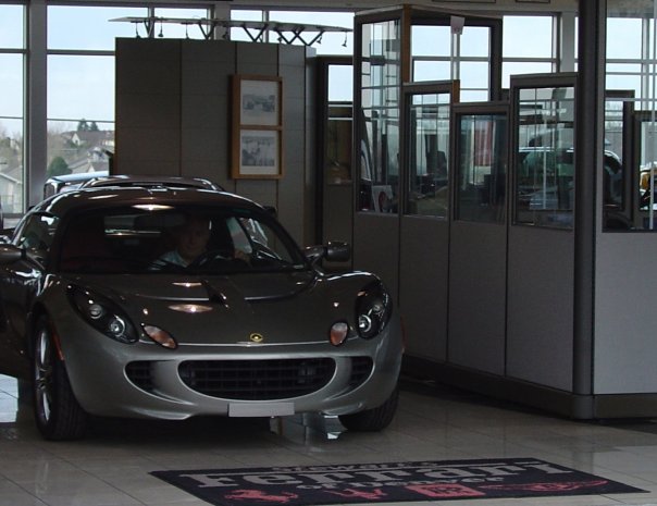 Silver Lotus Elise front view in a showroom with a driver seated inside