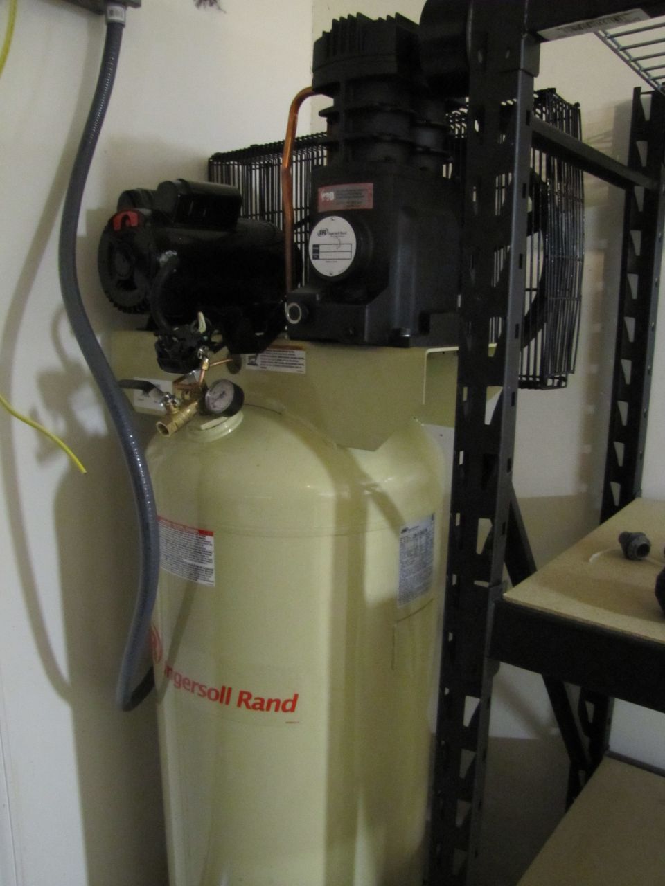 Yellow Ingersoll Rand air compressor with black motor and copper piping, next to a black metal shelf