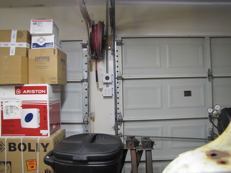 Boxes stacked high, a hose reel, and garage doors in a cluttered garage