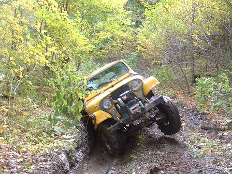 1978 Ford Bronco - A yellow jeep navigates a challenging muddy off-road path surrounded by autumn foliage.