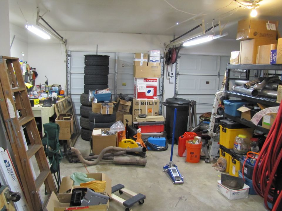 Garage interior with stacked tires, boxes, and exhaust pipes. Some readable text visible