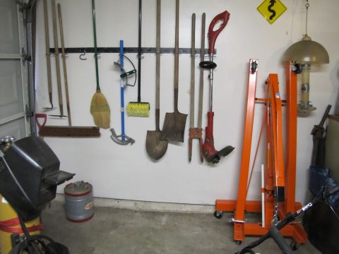 1993 Ford F-250 - A collection of garden tools and a welding machine are organized on a garage wall, with an engine hoist nearby.