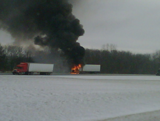 Two trucks on fire with black smoke billowing into the sky