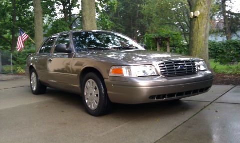 2007 Ford Crown Victoria - A 2007 Ford Crown Victoria is parked outside on a wet driveway with trees and an American flag in the background.