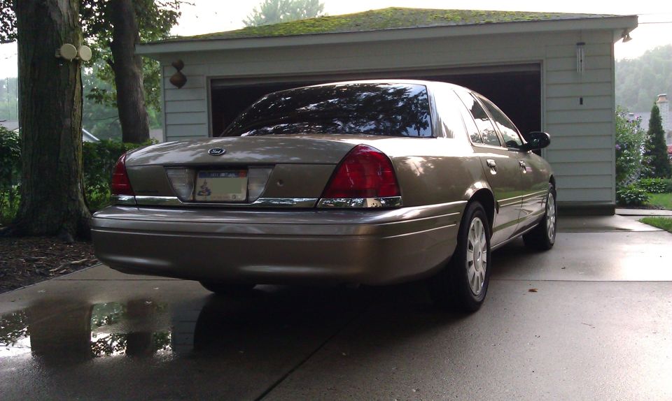 Rear view of a gold 2007 Ford Crown Victoria parked in a driveway in front of a garage