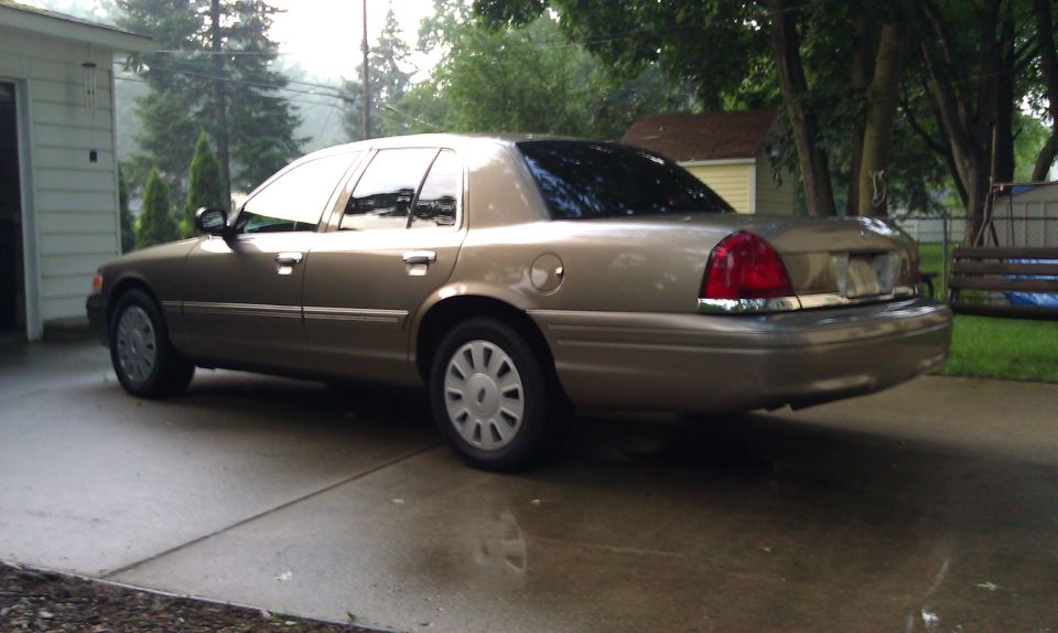 Tan 2007 Ford Crown Victoria parked on a wet driveway, viewed from the rear three-quarter angle