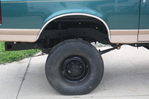 1996 Ford Bronco - The rear wheel and suspension system of a two-tone truck is shown from the side.