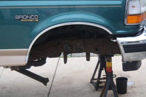 1996 Ford Bronco - The rear section of a teal 1996 Ford Bronco Eddie Bauer is shown on jack stands, revealing a heavily rusted frame.
