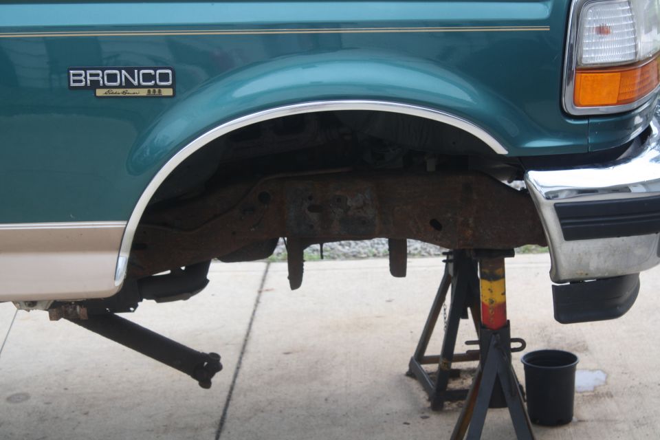 Teal 1996 Ford Bronco Eddie Bauer rear quarter panel and frame on jack stands, showing significant rust