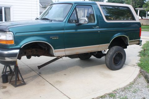 1996 Ford Bronco - A green 1996 Ford Bronco is elevated on jack stands, showing its undercarriage during a repair or build.
