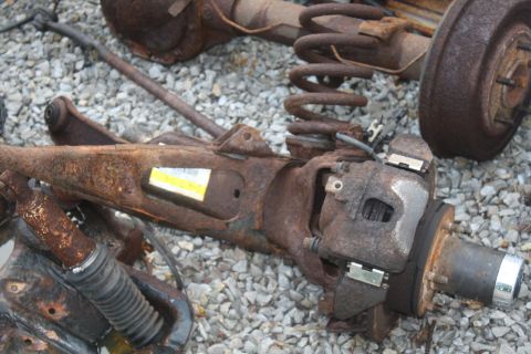 1996 Ford Bronco - Disassembled vehicle suspension parts lie on a gravel surface, showing significant rust and wear.