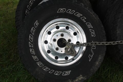 1996 Ford Bronco - Four Bridgestone Dueler A/T tires on chrome wheels are stacked and chained together.