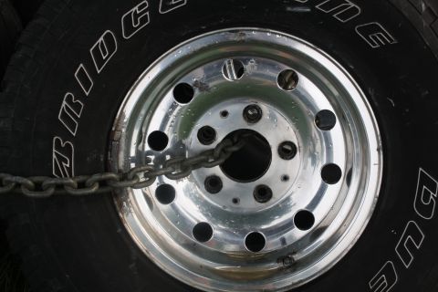1996 Ford Bronco - A heavy chain is wrapped around the lug nuts of a tire and chrome wheel assembly.