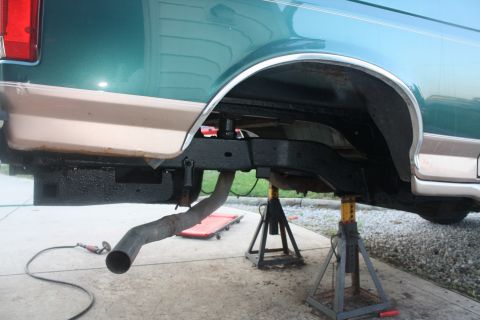 1996 Ford Bronco - The rear undercarriage of a truck is supported by jack stands, with an exhaust pipe visible.