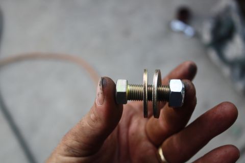 1996 Ford Bronco - A close-up shows a bolt with nuts and washers, held by a hand, against a blurred background.