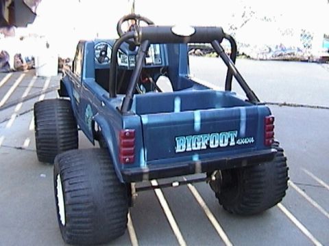 1985 Ford F-150 - A blue toy truck with "BIGFOOT 4X4" graphics is shown from the rear with large tires.