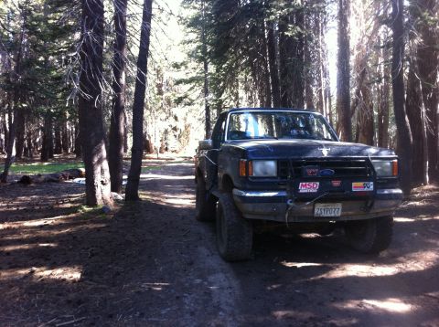1990 Ford Bronco - 1990 Ford Bronco parked on a dirt road in a forest.