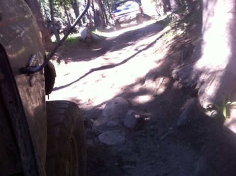 1990 Ford Bronco - Two vehicles navigate a rocky, wooded trail during an off-road excursion.