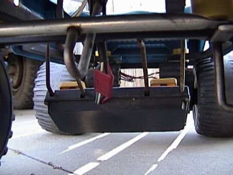 1985 Ford F-150 - The underside of a lawn mower deck is shown, with its exhaust pipe and rear wheels visible.