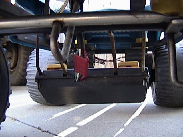 Underside of a lawn mower deck with exhaust pipe and wheels visible