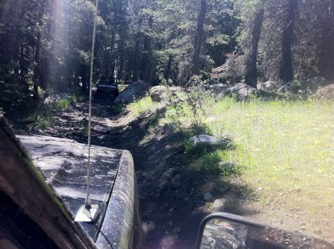 1990 Ford Bronco - Two SUVs navigate a challenging dirt path surrounded by trees and large rocks.