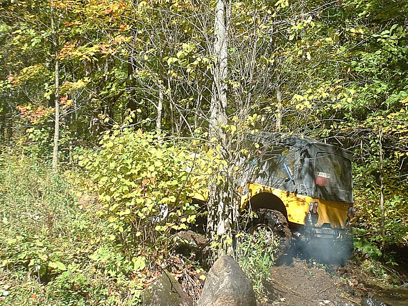 Yellow off-road vehicle with a camouflage top stuck in mud and trees