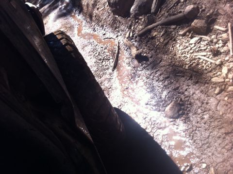 1990 Ford Bronco - A vehicle navigates a muddy, rocky trail with a visible tire and the ground ahead.