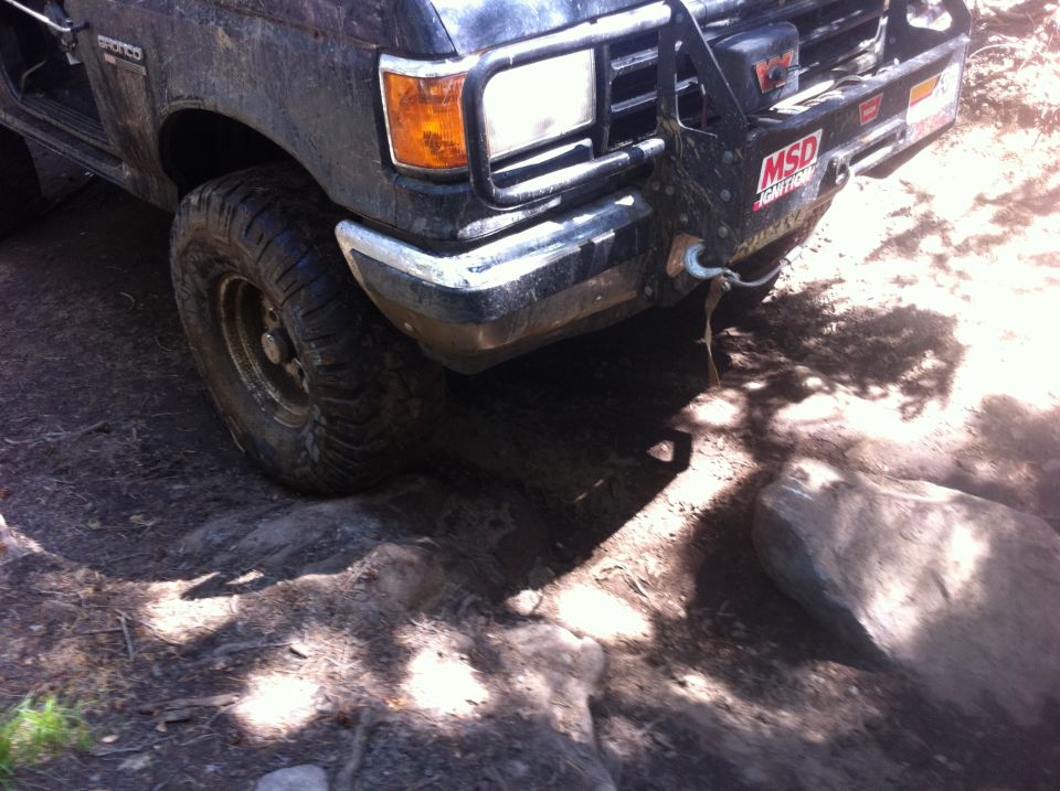 Front of a dark-colored off-road vehicle with a winch and brush guard, navigating over rocks